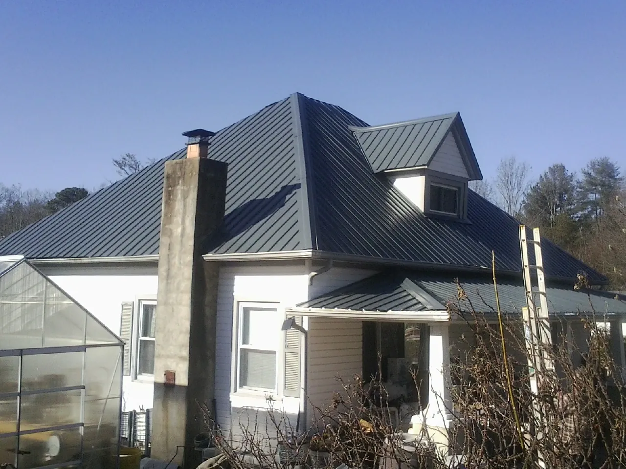 Dark blue standing seam metal roof on a white farmhouse with dormer — Slate & Tile Roof Repair by Roofing Brothers in Okeechobee